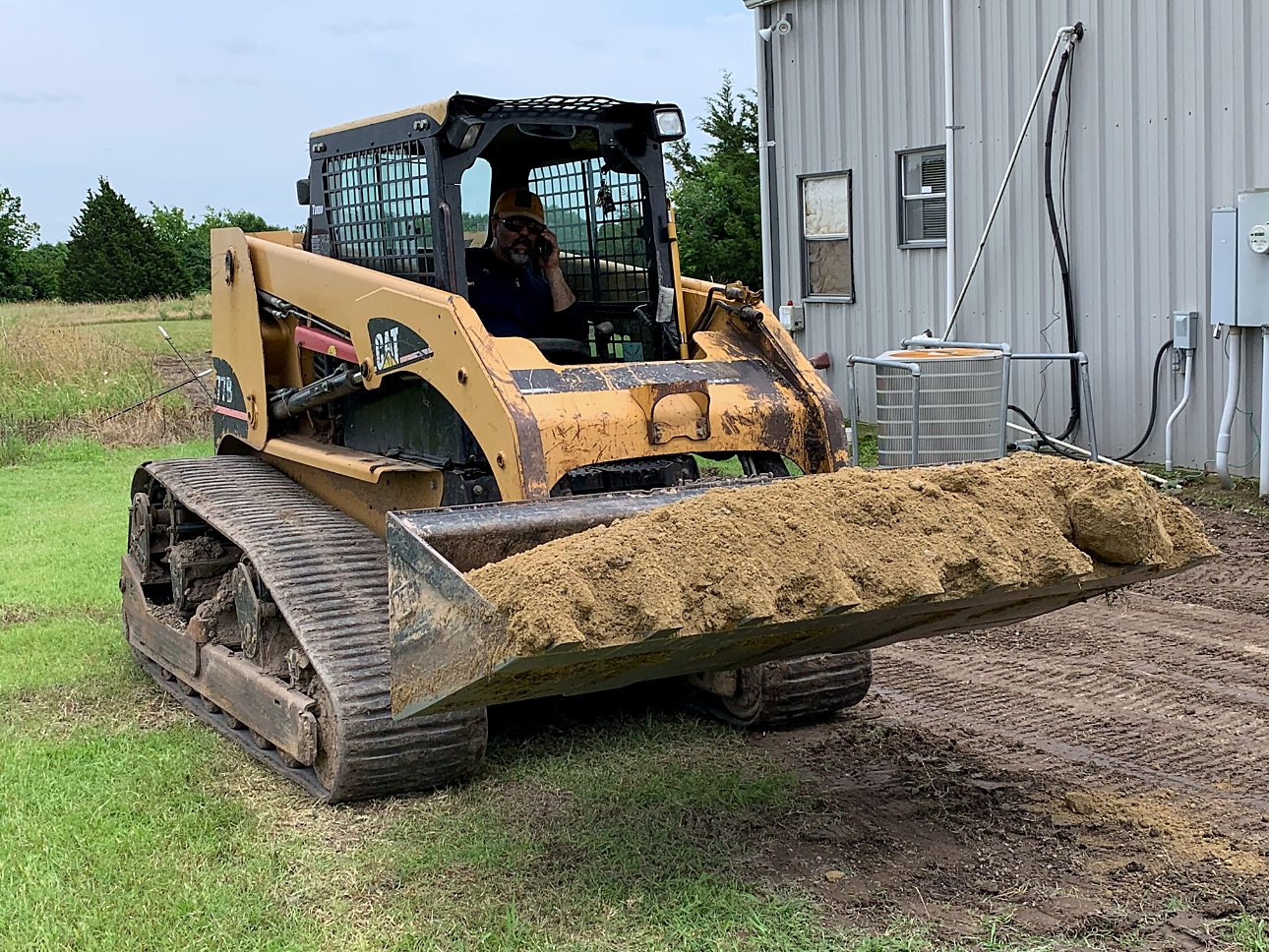 Roland in a yellow skid loader with a bucket of dirt