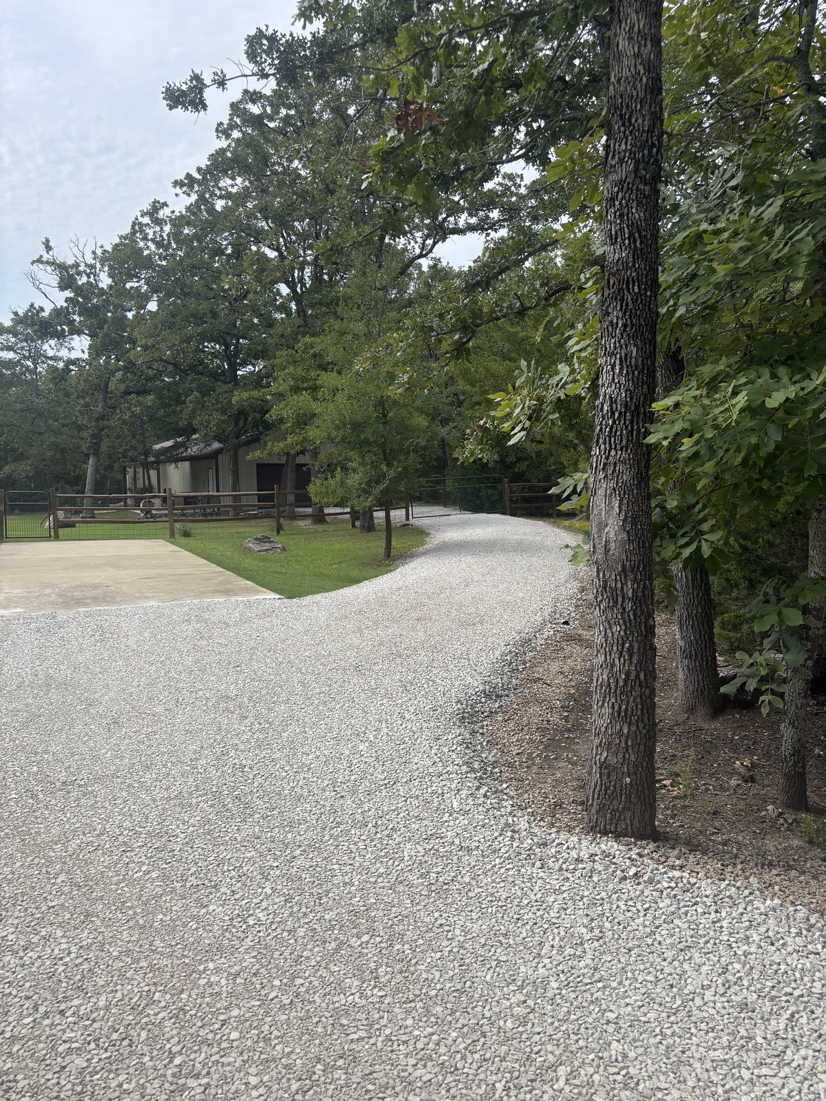 Freshly graded light gravel driveway curving past a wooden fence toward a tan building