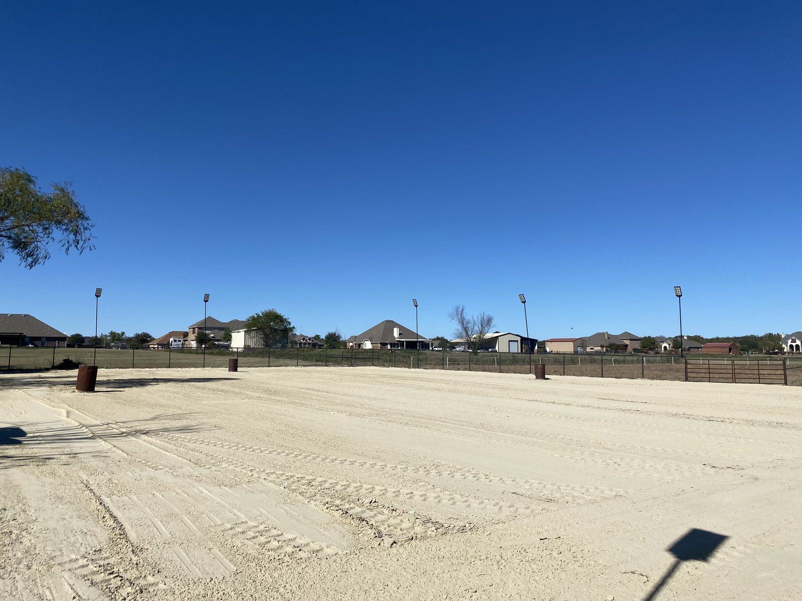 Horse arena grading with light poles, barrels, and a wooden gate