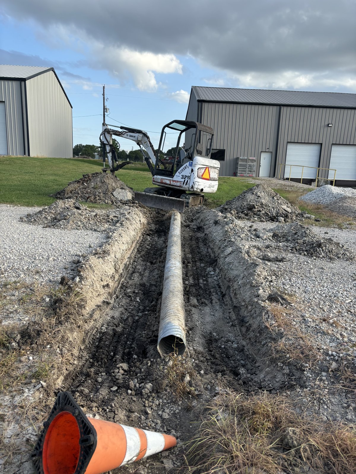 Bobcat excavator in a trench with a corrugated metal culvert pipe