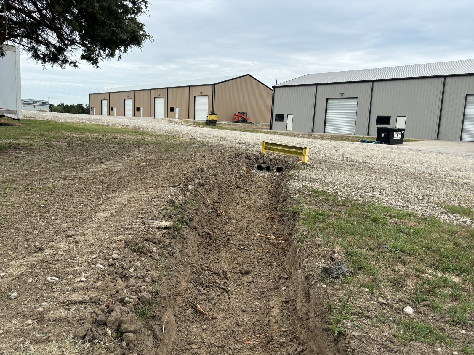 Drainage trench leading to black culvert pipes under a yellow guardrail
