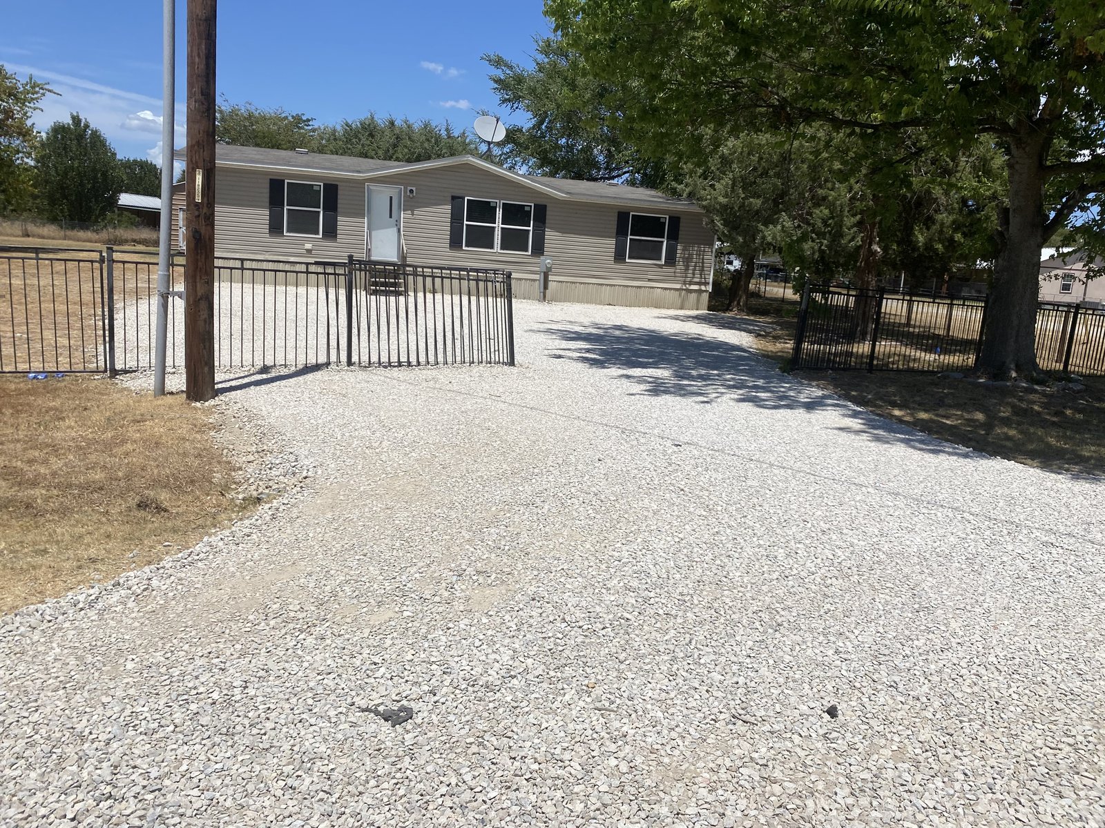Fresh gravel driveway leading to a tan manufactured home