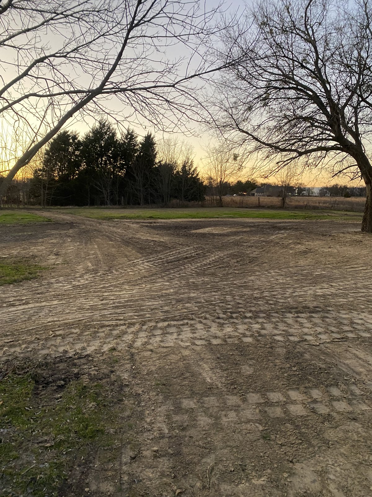 Cleared and graded dirt lot with track marks at sunset