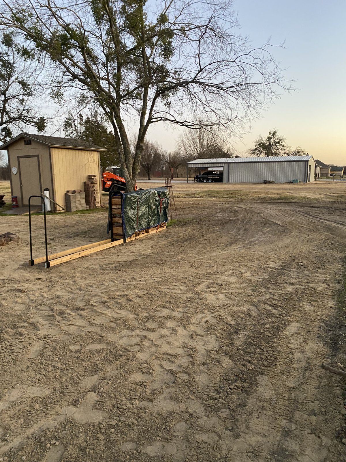 Graded backyard with shed, firewood, and an orange Kubota nearby