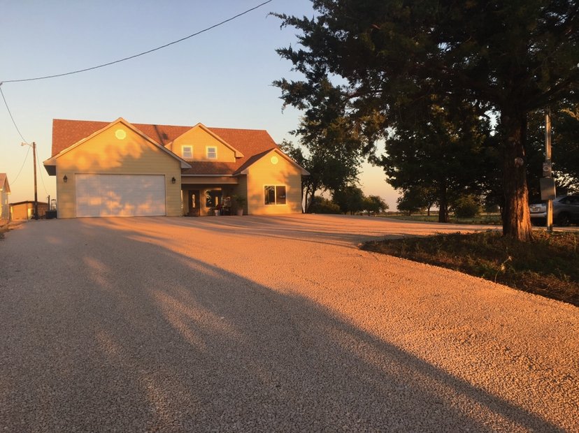 Fresh gravel driveway in front of a yellow two-story house at golden hour