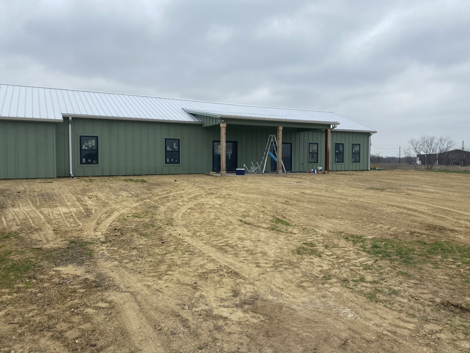 Graded dirt lot in front of an olive-green barndominium