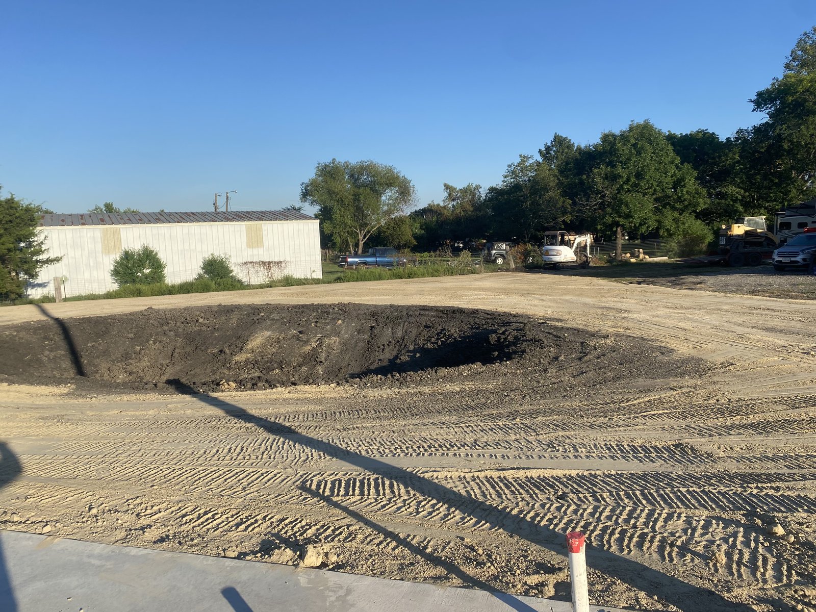 Leveled sandy pad with dark soil fill and equipment in the background