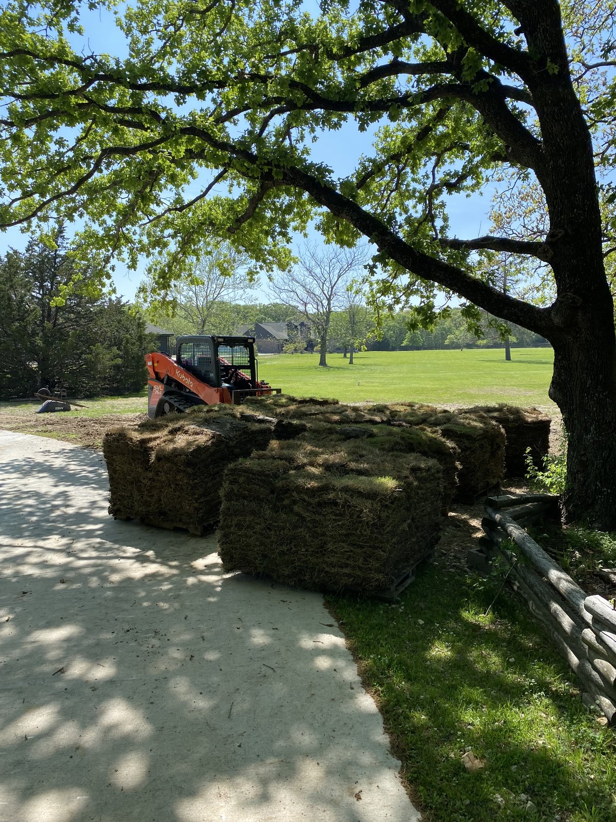 Pallets of sod and an orange Kubota loader on a driveway