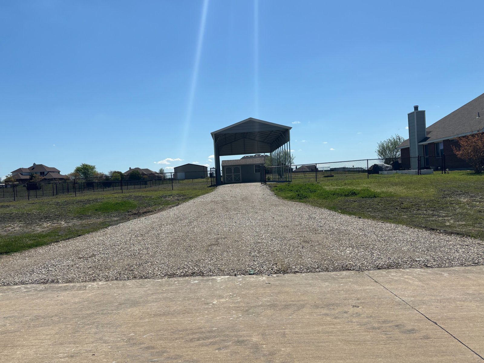 Fresh gravel driveway leading to a metal carport and shed