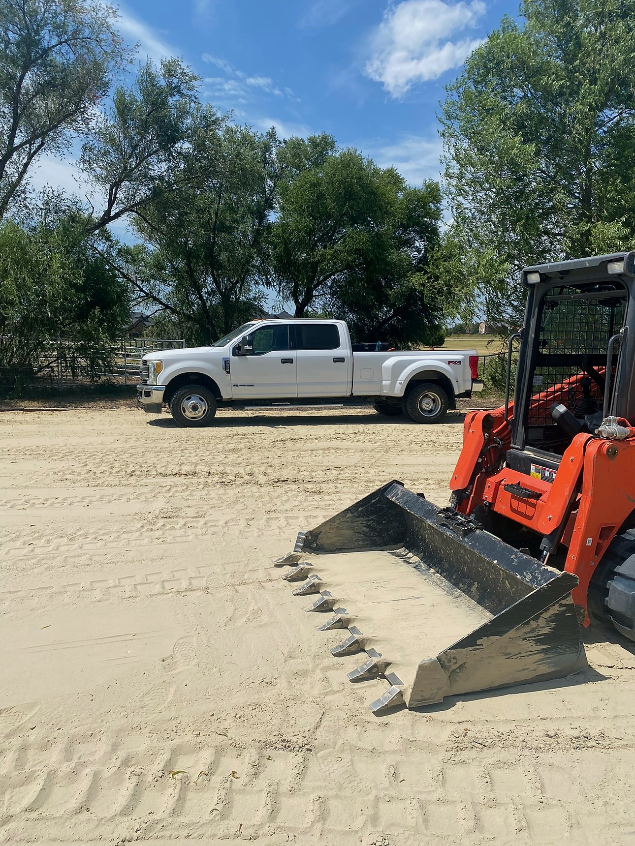 Orange loader bucket and white Ford dually on a job site